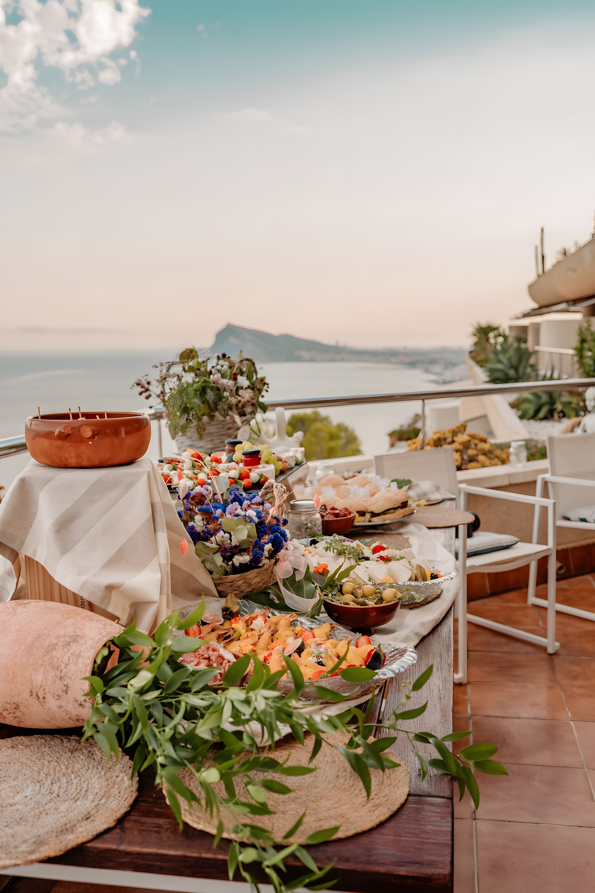 A tiered table of food and flowers on a terrace overlooking the bay