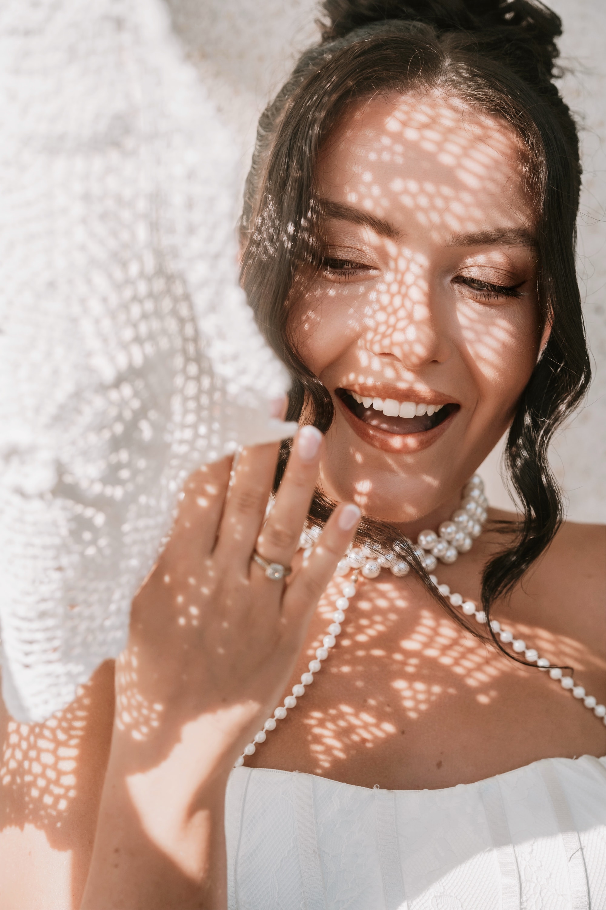 A bride laughing in dappled sunlight, wearing pearls